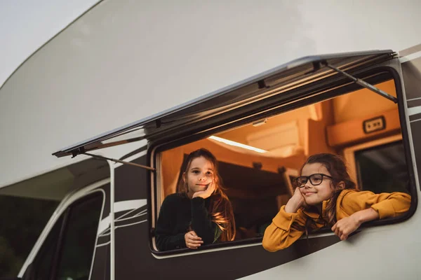 Glada små flickor tittar ut genom husvagn fönster på kvällen, familj semester resa. — Stockfoto