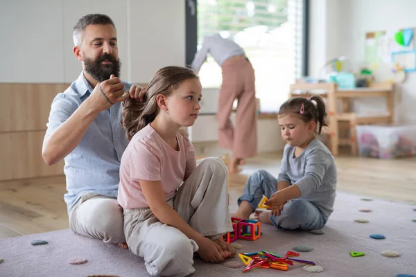 Vater mit drei Töchtern zu Hause, spielt und macht Haare. — Stockfoto