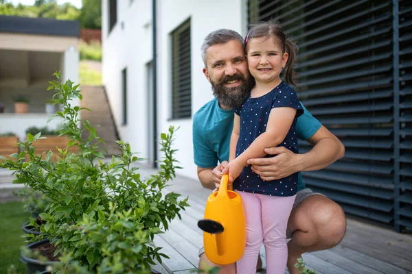 Otec a malá dcera s konvicí na vodu venku na dvorku, dívají se na kameru. — Stock fotografie