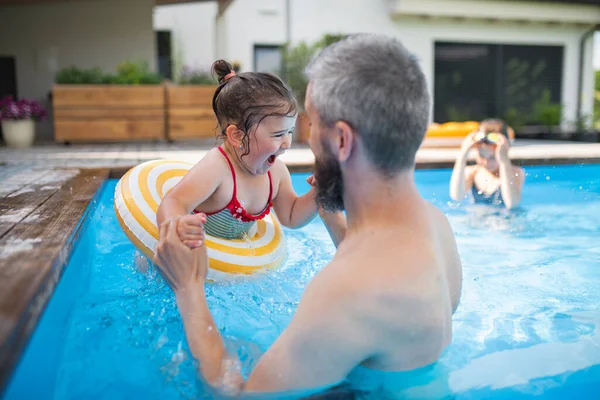 Padre con hijas al aire libre en el patio trasero, jugando en la piscina. — Foto de Stock