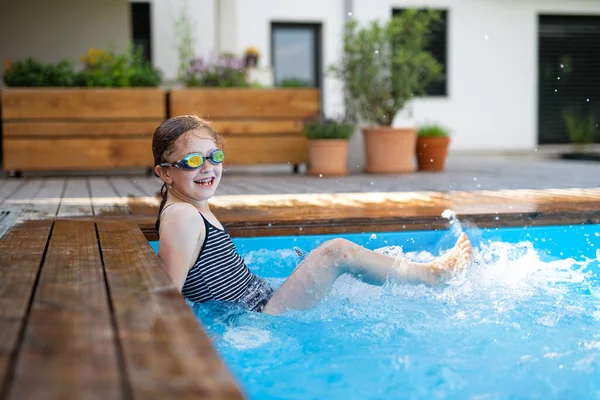 Arka bahçede gözlüklü küçük bir kız yüzme havuzunda oturuyor ve kameraya bakıyor.. — Stok fotoğraf