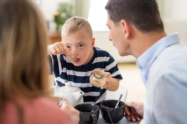 Família feliz com síndrome de down filho na mesa, tomando café da manhã. — Fotografia de Stock