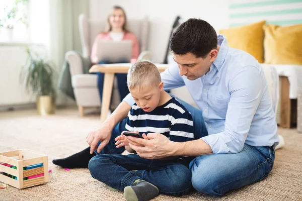Ayah dengan bahagia turun sindrom anak di dalam rumah, menggunakan smartphone. — Stok Foto