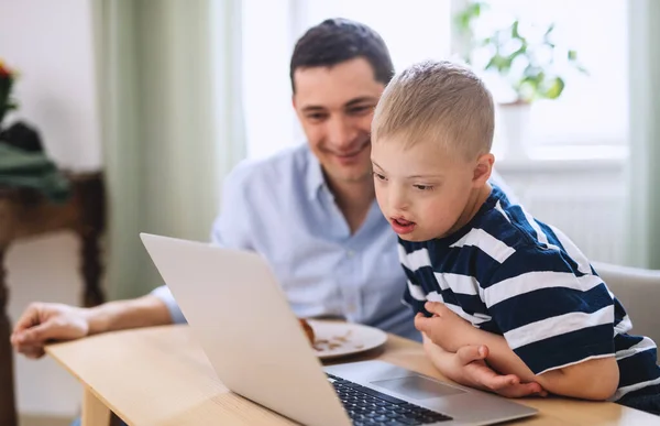 Far med happy down syndrom son inomhus, med hjälp av laptop. — Stockfoto