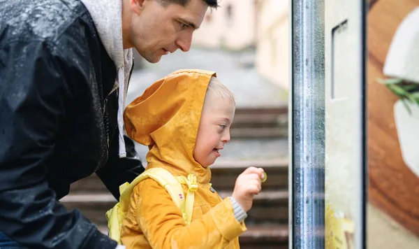 Szczęśliwy chłopiec z zespołem Downa z ojcem na zewnątrz na spacerze w deszczu, bawiąc się. — Zdjęcie stockowe