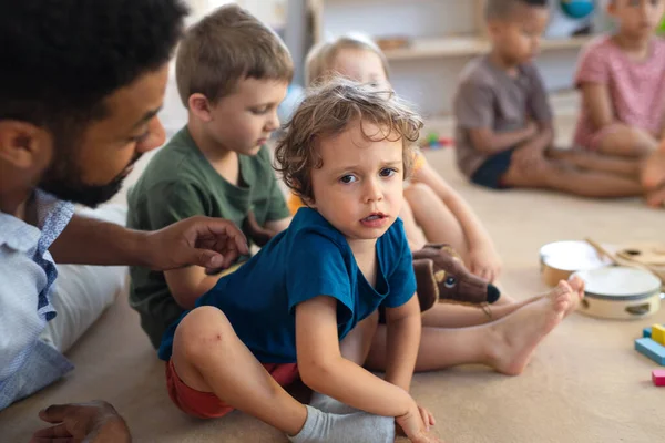 Mann Lehrer spricht mit kleinen unglücklichen Jungen drinnen im Klassenzimmer und tröstet ihn. — Stockfoto