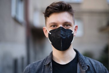 Şehrin caddesinde yürüyen ve kameraya bakan genç adamın ön görüntüsü, koronavirüs konsepti.