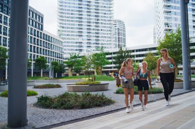 Bir grup genç ve yaşlı kadın, egzersizden sonra şehirde yürüyorlar ve konuşuyorlar..