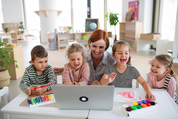 Groep kleine kleuterschoolkinderen met leraar in de klas, met laptop. — Stockfoto