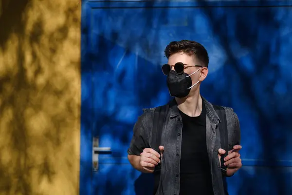 Портрет молодого человека в солнечных очках, стоящего на открытом воздухе на синем фоне, коронавирусная концепция. — стоковое фото