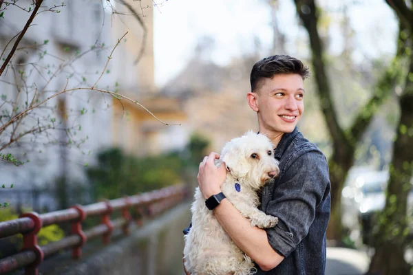 Retrato de jovem caminhando ao ar livre na rua na cidade, segurando cão. — Fotografia de Stock