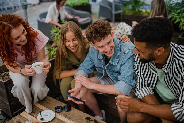 Skupina šťastných mladých lidí sedících venku v kavárně na výletě do města a bavících se. — Stock fotografie