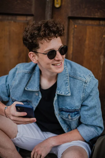 Retrato de jovem feliz ao ar livre na frente da porta, usando smartphone. — Fotografia de Stock