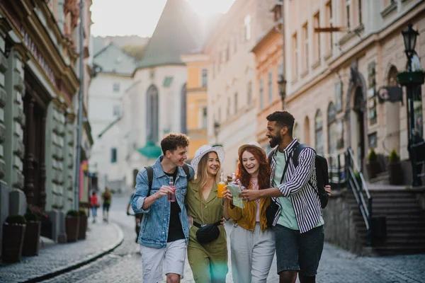 Frontansicht einer Gruppe glücklicher junger Leute im Freien auf einem Stadtausflug, die mit Getränken spazieren gehen. — Stockfoto