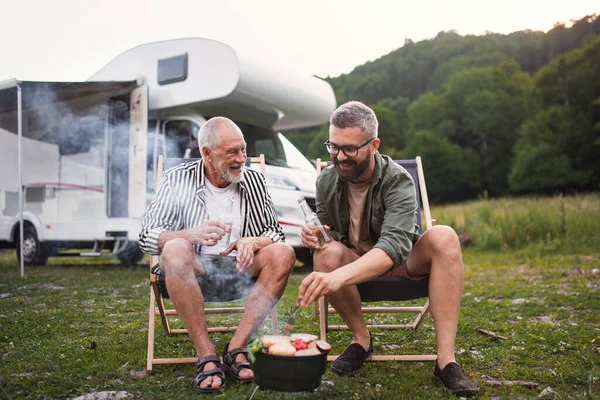 Mature man with senior father talking at campsite outdoors, barbecue on caravan holiday trip. — Stock Photo, Image