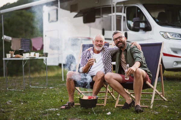 아버지와 함께 야외 야영지에서 카메라를 보고 있는 성숙 한 남자, 캐러 밴 휴가 여행에서 바베큐를 하는 모습. — 스톡 사진