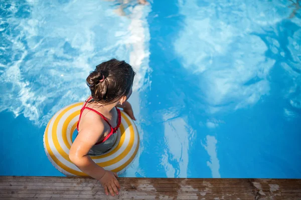 Vista superior de la niña pequeña al aire libre en el patio trasero, con anillo de goma en la piscina. —  Fotos de Stock