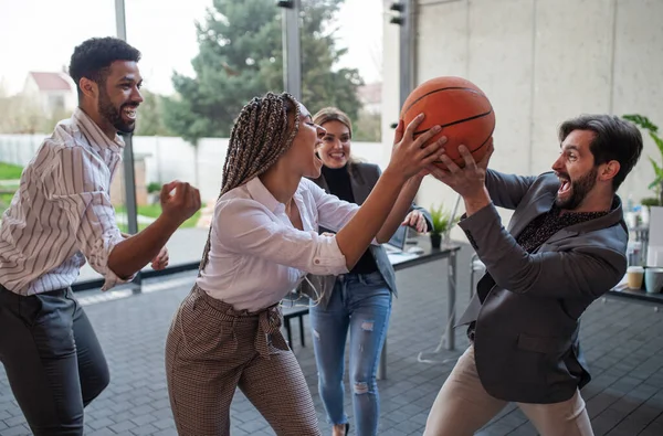 Группа веселых молодых бизнесменов, играющих в баскетбол в офисе, берёт перерыв. — стоковое фото