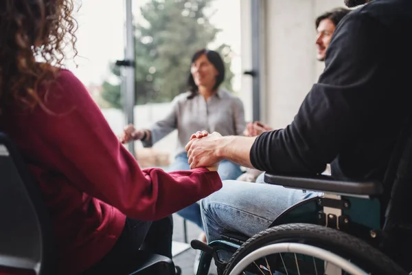 Αγνώριστοι άνδρες και γυναίκες με αναπηρική καρέκλα που κάθονται σε κύκλο κατά τη διάρκεια της ομαδικής θεραπείας, κρατώντας τα χέρια. — Φωτογραφία Αρχείου