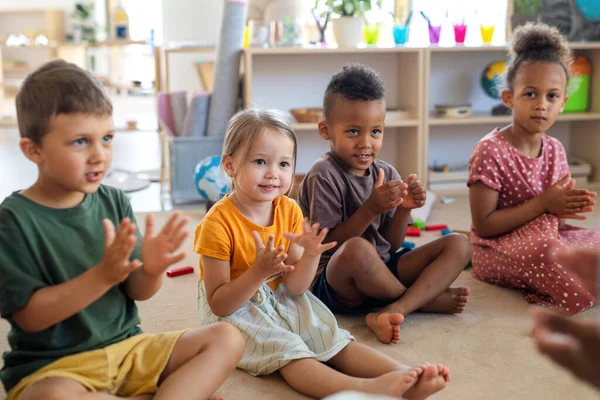 Gruppo di piccoli bambini della scuola materna seduti sul pavimento al chiuso in classe, applaudendo. — Foto Stock