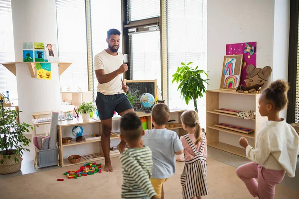 Gruppe kleiner Kindergartenkinder mit einem männlichen Lehrer, der drinnen im Klassenzimmer steht und Sport macht. — Stockfoto