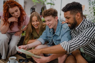 Bir grup mutlu genç şehir gezisinde açık kafede oturuyor, harita kullanarak..