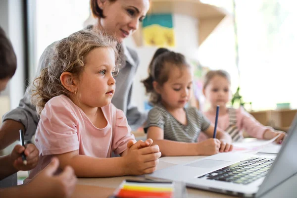 Група маленьких дітей дитячої школи з учителем в приміщенні в класі, використовуючи ноутбук . — стокове фото