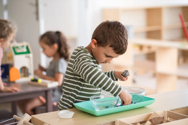 Petit garçon d'école maternelle jouant à l'intérieur dans la salle de classe, apprentissage montessori. — Photo