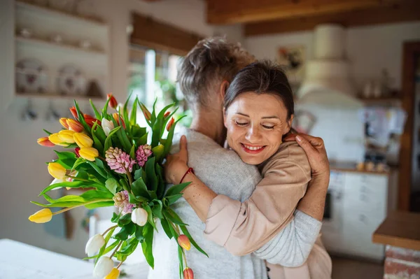 Mãe sênior feliz abraçando a filha adulta dentro de casa, dia das mães ou celebração de aniversário. — Fotografia de Stock