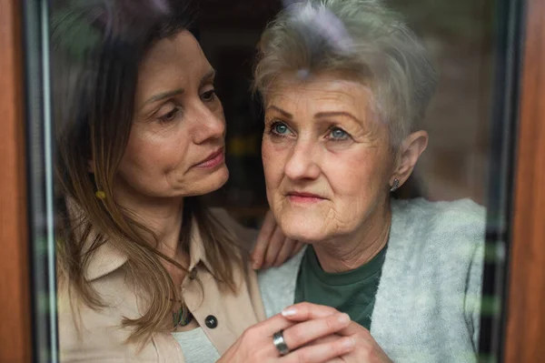 Close-up portrait of sad senior mother with adult daughter indoors at home, hugging. — Stock Photo, Image