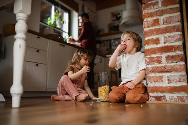 Two small children with father indoors at home, eating cornflakes on floor. — Stock Photo, Image