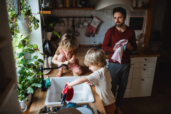 Зрелый отец с двумя маленькими детьми, мыть посуду в помещении дома, ежедневные обязанности концепция. — стоковое фото
