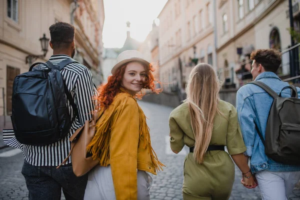 Visão traseira do grupo de jovens felizes ao ar livre em viagem na cidade, andando e olhando para trás. — Fotografia de Stock