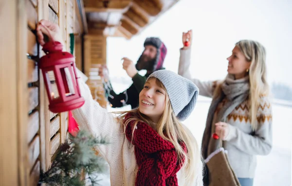 Família com a pequena filha que decora o terraço da casa ao ar livre no inverno, tempo de Natal. — Fotografia de Stock