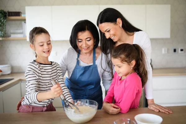 Chicas pequeñas felices con la madre y la abuela haciendo mezcla de panqueques en el interior de casa, cocinar. —  Fotos de Stock