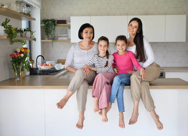 Щасливі маленькі дівчата з матір'ю і бабусею сидять на кухонній стійці вдома, дивлячись на камеру . — стокове фото