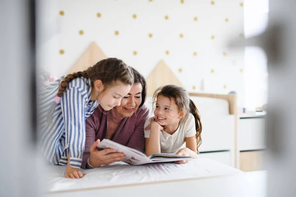Щасливі маленькі дівчата з бабусею в приміщенні в спальні вдома, читання на ліжку . — стокове фото