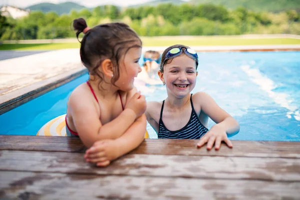 Dos hermanas niñas pequeñas al aire libre en el patio trasero, hablando en la piscina. — Foto de Stock