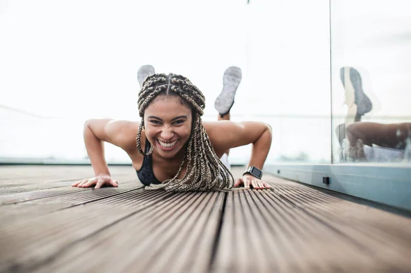Молодая женщина делает упражнения и смотрит на камеру на открытом воздухе на террасе, спорт и здоровый образ жизни. — стоковое фото