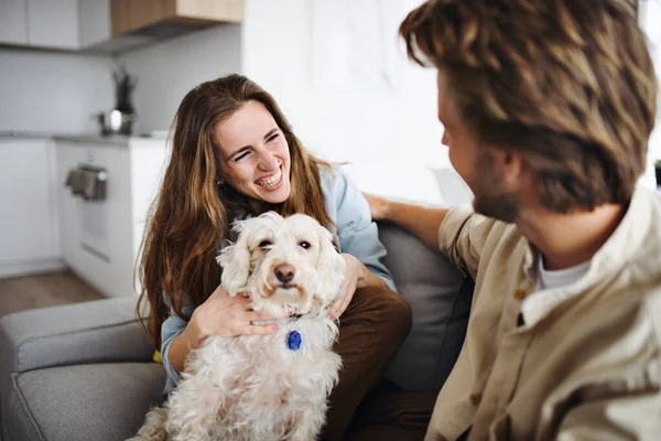 Felice giovane coppia innamorata di cane seduto sul divano in casa, a riposo. — Foto Stock