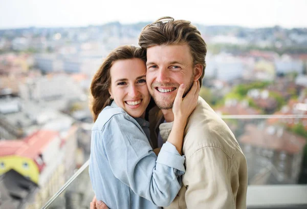 Joyeux jeune couple amoureux regardant la caméra à l'extérieur sur le balcon à la maison, étreignant. — Photo