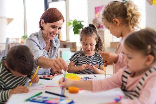 Ομάδα μικρών παιδιών νηπιαγωγείου με δάσκαλο σε εσωτερικούς χώρους στην τάξη, ζωγραφική. — Φωτογραφία Αρχείου