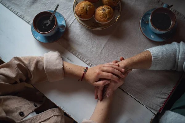 Vista superior de la madre mayor tomando café con la hija adulta en el interior de casa, tomados de la mano. — Foto de Stock