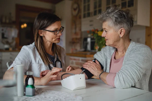 Trabalhador de saúde ou cuidador visitando a mulher idosa em casa, medindo a pressão. — Fotografia de Stock