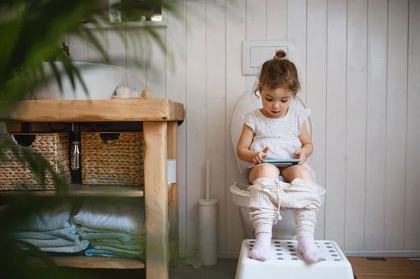 Retrato de lindo pequeño sentado en el inodoro en el interior de casa, utilizando el teléfono inteligente. — Foto de Stock