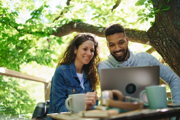 Glückliches Paar mit Laptop im Freien in einem Baumhaus, Wochenendausflug und abgelegenem Bürokonzept. — Stockfoto