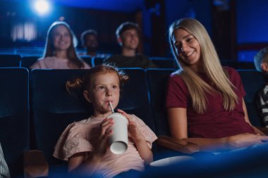 Anne ve küçük mutlu çocuklar sinemada, film izliyor ve pipetle içiyor..