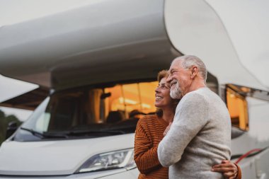 Kıdemli çift akşam karanlığında ayakta ve dışarıda sarılıyorlar, karavan tatili gezisi..