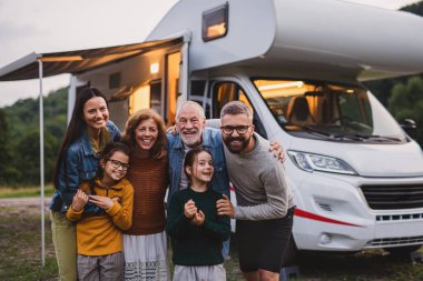 Günbatımında dışarıda kameraya bakan çok nesilli bir aile, karavan gezisi..