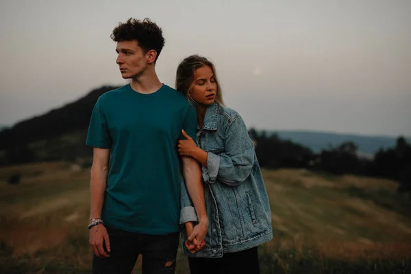 Pareja joven de pie en la naturaleza en el campo, tomados de la mano, pero mirando el uno al otro. —  Fotos de Stock